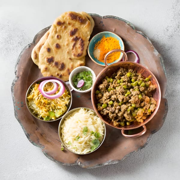 An Indian meal with naan, rice, keema matar, and spices on a rustic tray.